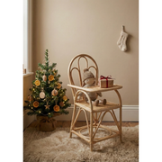 Wooden high chair with a teddy bear and small gift, Christmas tree with decorations in a room.