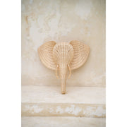 Frontal view of the rattan elephant wall hanging against a stone-toned wall