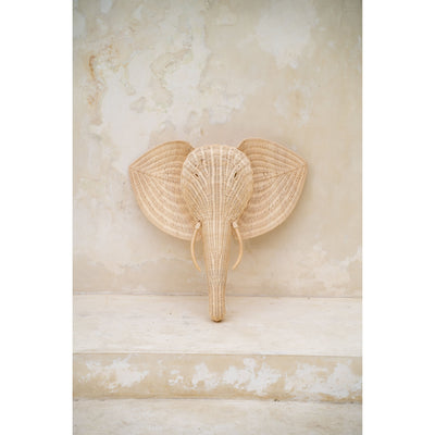 Frontal view of the rattan elephant wall hanging against a stone-toned wall