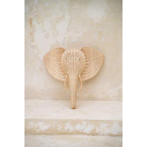 Frontal view of the rattan elephant wall hanging against a stone-toned wall