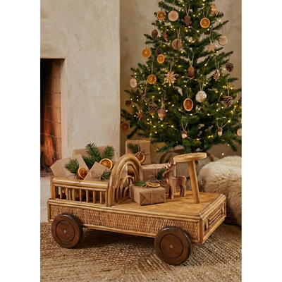 Wooden toy cart with Christmas decorations in front of a decorated tree and fireplace.