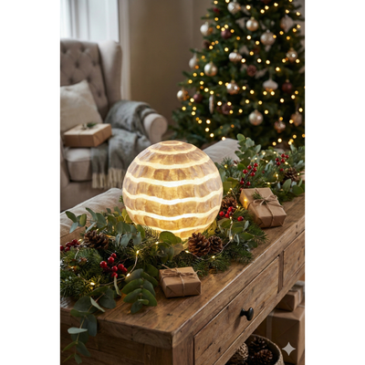Decorative table with a glowing spherical lamp, Christmas tree, and presents in a cozy living room.