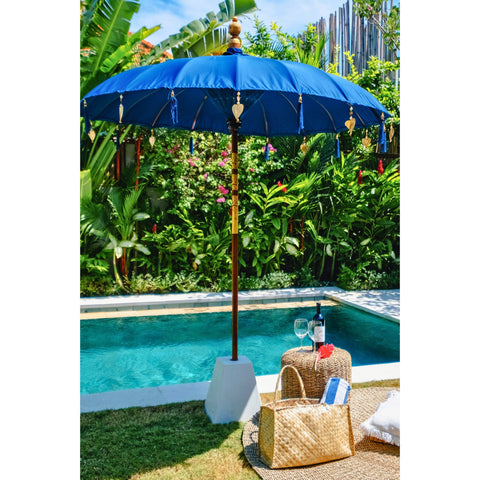 The Coastal Blue Parasol styled poolside with wine glasses and woven stools for a relaxed outdoor setting.