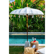 Full white parasol standing tall by the pool with rich tropical greenery and red-tiled roofs in the background.
