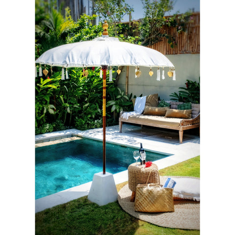 Side angle shot of the white parasol poolside next to a daybed and tropical garden, capturing lifestyle setup and bright lighting.