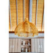 Frilly rattan lampshade hanging from wooden and rattan ceiling in rustic cottage. Lighting by Collectiviste.